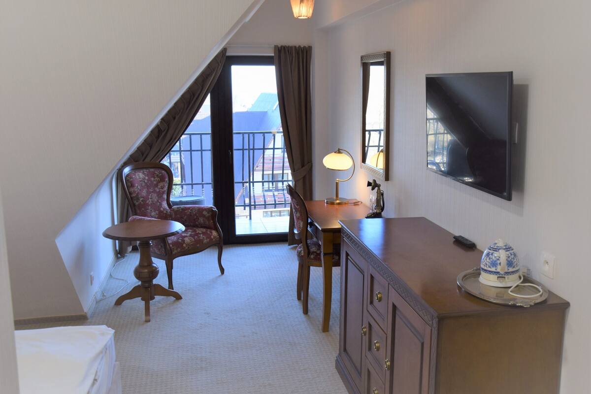 Een hotelkamer met balkon, televisie, bureau met lamp, stoel en dressoir.