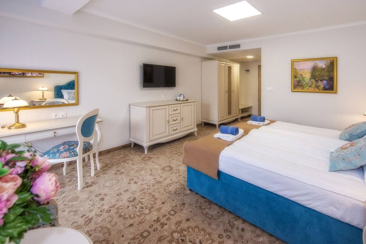 Een hotelkamer met een bed, een bureau met stoel, een kledingkast, een televisie en een schilderij aan de muur.