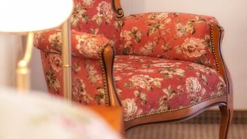 Een fauteuil met bloemenprint en houten frame, een vloerlamp en een bed met bloemenbedekking.