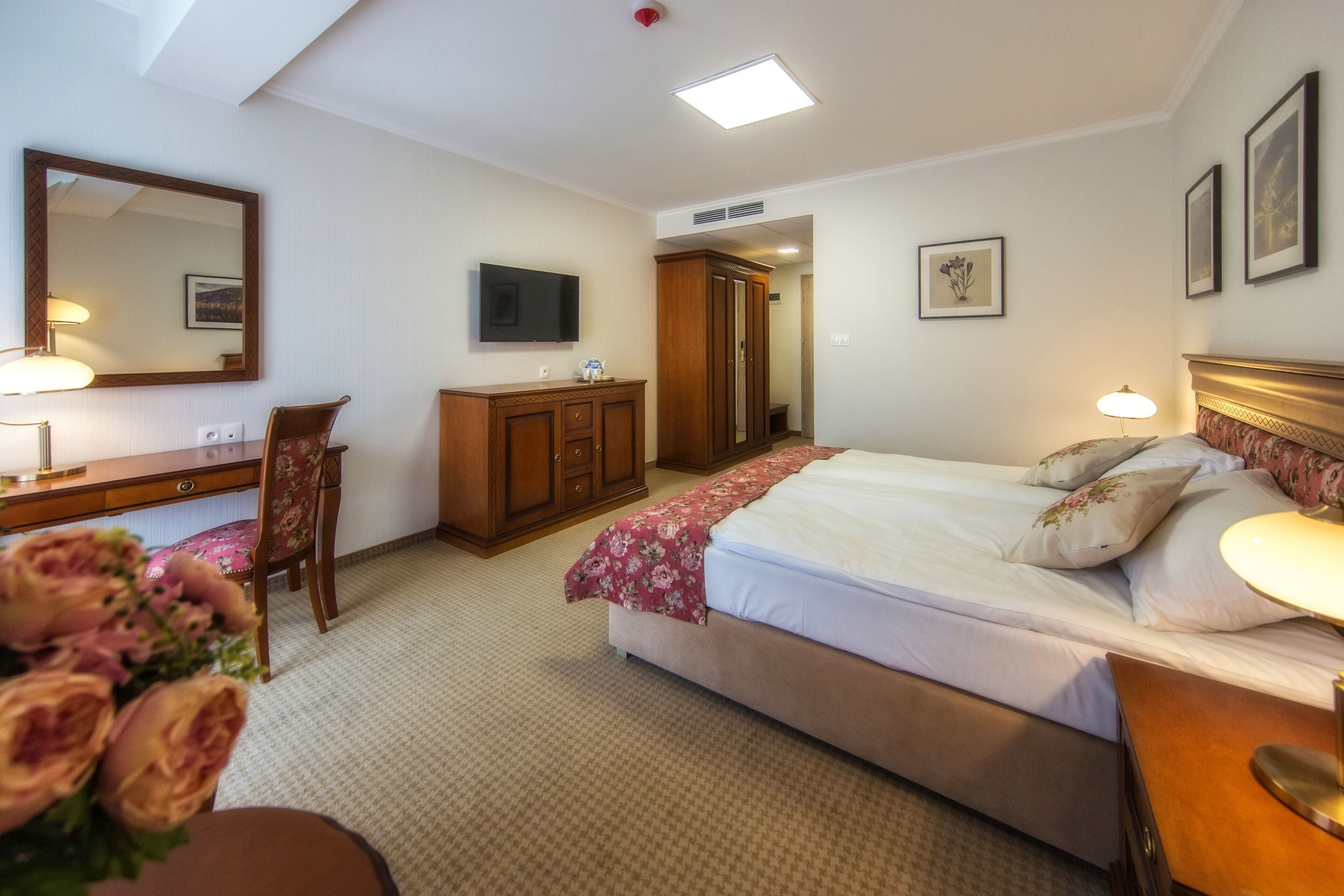 Una habitación de hotel con cama, mesita de noche, lámpara, cómoda, espejo y televisor.