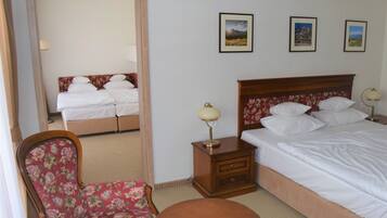 A hotel room with a bed, a chair, a table, and three framed pictures on the wall.