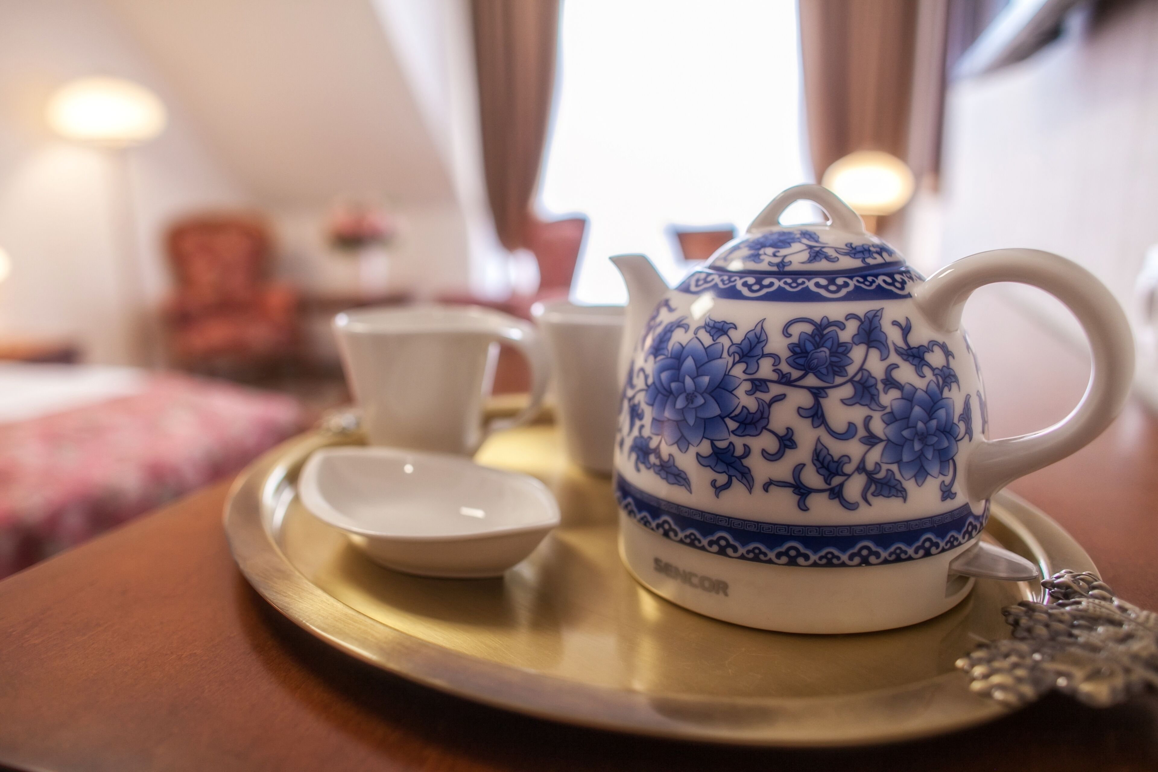 A tea set on a tray in a room with a bed and a lamp in the background.