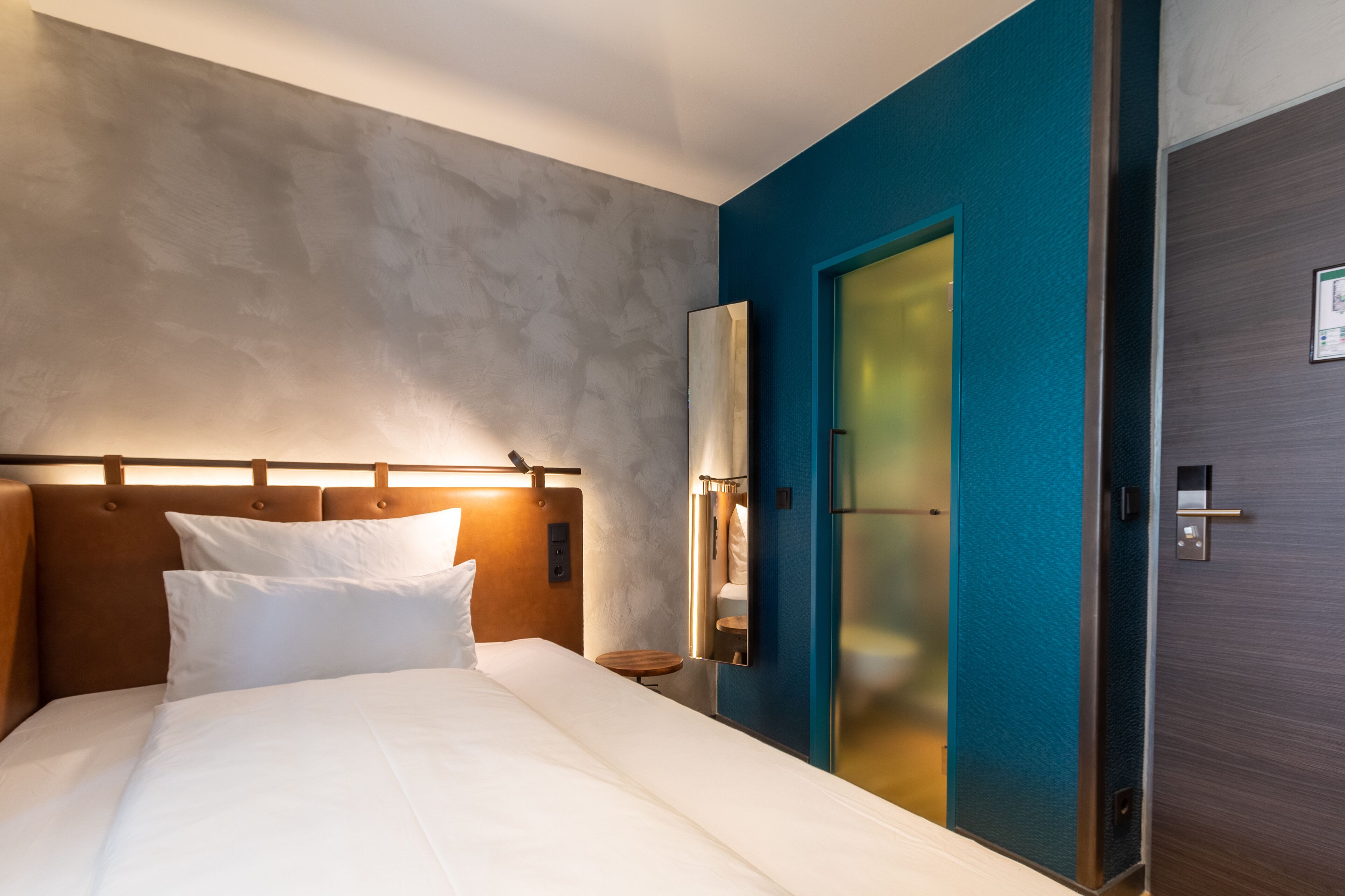 A hotel room with a bed, a nightstand, a mirror, and a door.