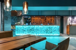 A modern bar area with a glowing blue light feature, wooden accents, and a seating area with a wooden table and chairs.