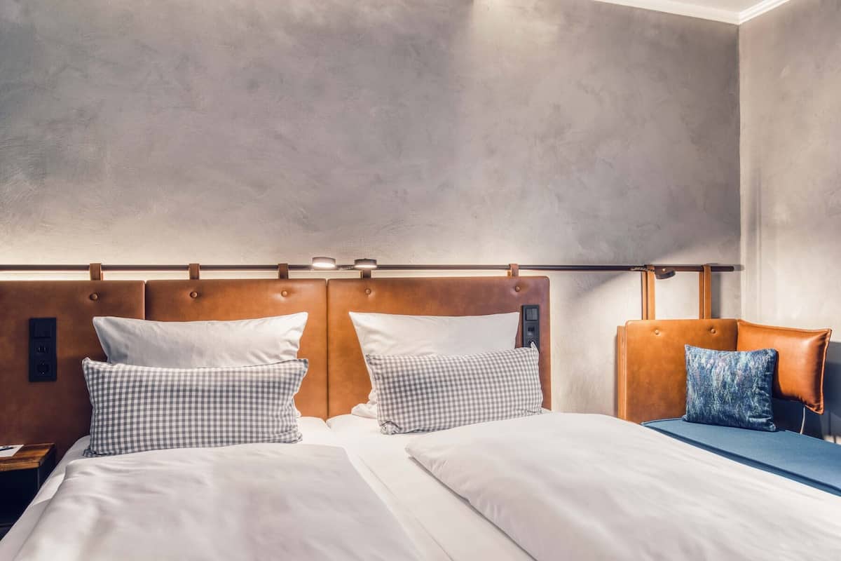 Una habitación de hotel con una cama grande, dos almohadas, un cabecero y una mesita de noche.