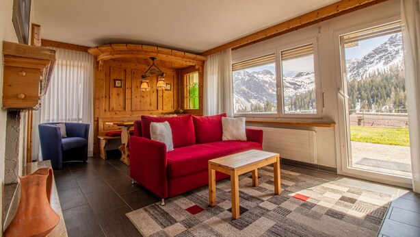 A cozy room with a red sofa, wooden walls, a dining area, and a view of mountains. - Villa Franca UO (Arosa)