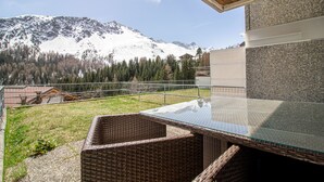 A balcony with wicker furniture, a glass table, and a view of snow-covered mountains. - Villa Franca UO (Arosa)