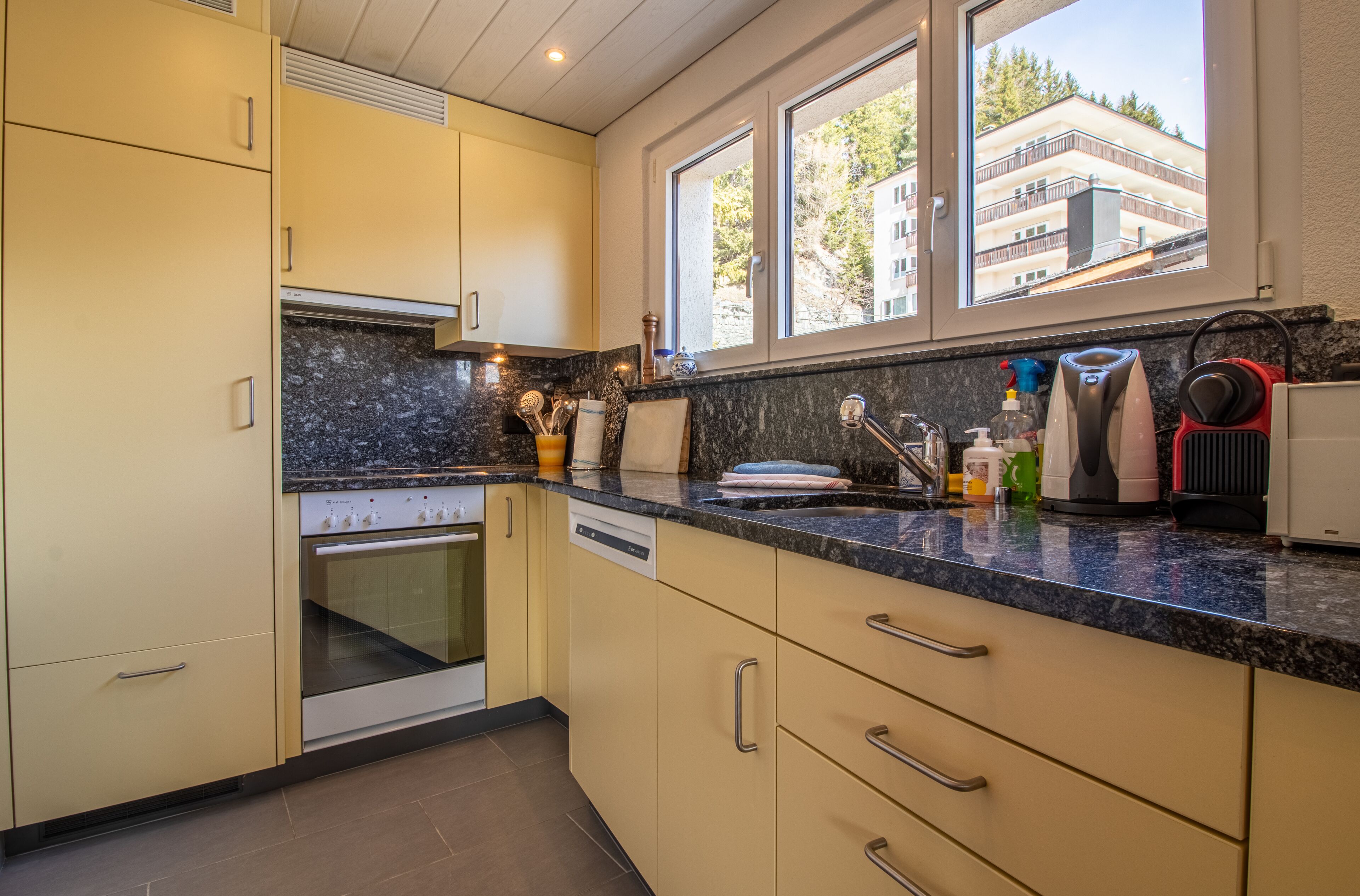 A modern kitchen with beige cabinets, a built-in oven, and a granite countertop.