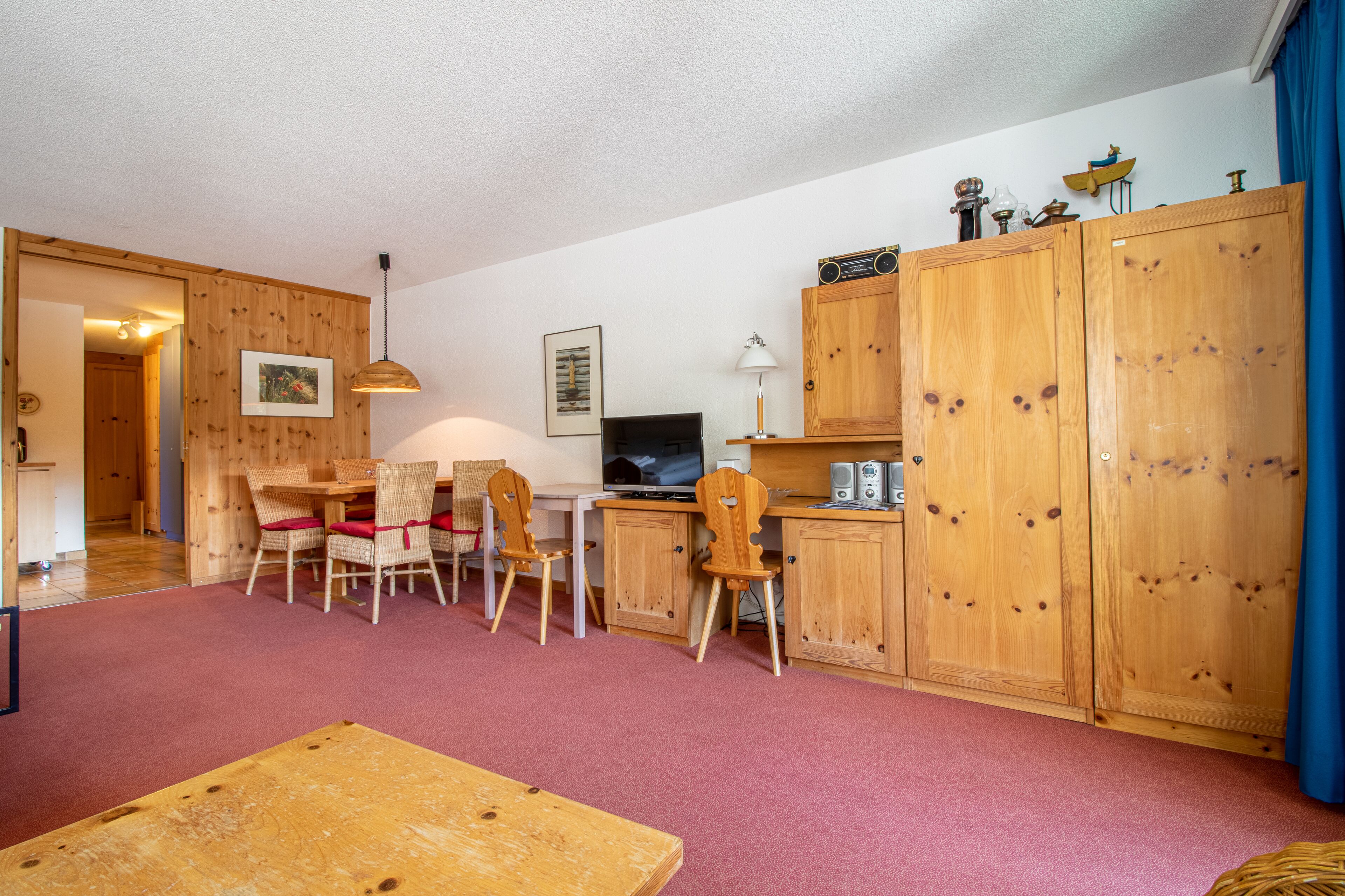 A cozy room with a wooden desk, chairs, a television, and a cabinet.