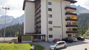 A multi-story hotel with balconies and a parking area in front. - Rothornblick 52 (Arosa)