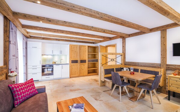 Un intérieur chaleureux avec une table à manger en bois, des chaises, un canapé et un coin cuisine équipé de placards et d’une cuisinière.