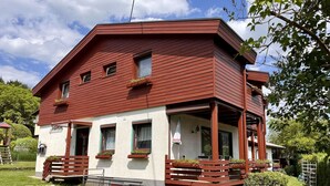 Un edificio a due piani con facciata rossa e pareti bianche, dotato di un balcone con ringhiera in legno e piante in vaso.