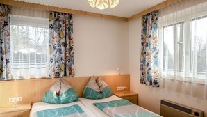 A bedroom with a bed, two bedside tables, a lamp, and a window with floral curtains.