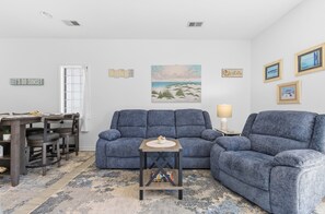 A living room with a blue sofa, a small table with a bowl, and a painting of a beach scene. - Quiet 2BR Golf Villa in Sunset Beach. (RP3209) (Sunset Beach)