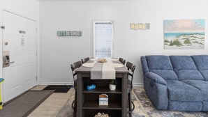 A dining area with a table, chairs, a blue sofa, and a painting on the wall.