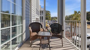 A balcony with wicker chairs and a small table, overlooking a parking area and trees.