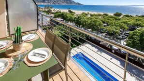 A balcony with a table set for dining, overlooking a beach and a pool. - Cosy apartment for 5 guests with WIFI, A/C, pool, TV and terrace (Roses)