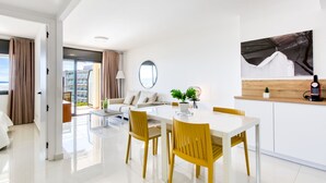 A modern hotel room with a dining area, a sofa, a coffee table, and a view of the cityscape. - Cosy apartment for 5 guests with WIFI, A/C, pool, TV and terrace (Roses)