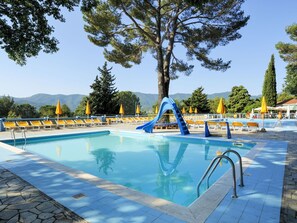 Ein Poolbereich mit einer blauen Rutsche, gelben Liegestühlen und Bergblick im Hintergrund.