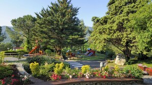 Ein Park mit Spielgeräten, einer Fußgängerampel und verschiedenen Bäumen und Blumen.