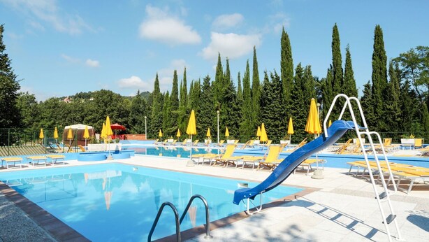 Ein Swimmingpool mit einer blauen Rutsche, gelben Sonnenschirmen und Liegestühlen.