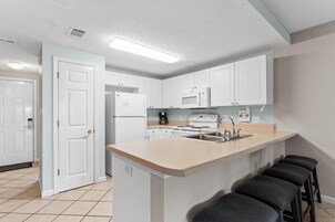 A modern kitchen with white cabinets, a central island with bar stools, a microwave, and a stove.