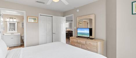 A bedroom with a bed, a ceiling fan, a television, a dresser, and a bathroom visible through an open door.
