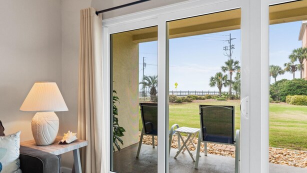 A room with a sliding glass door leading to an outdoor seating area with a table and chairs. - Ciboney Beach Resort Panhandle Getaways (Miramar Beach)