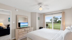 A bedroom with a bed, a television on a dresser, a ceiling fan, and a view of the outdoors. - Ciboney Beach Resort Panhandle Getaways (Miramar Beach)