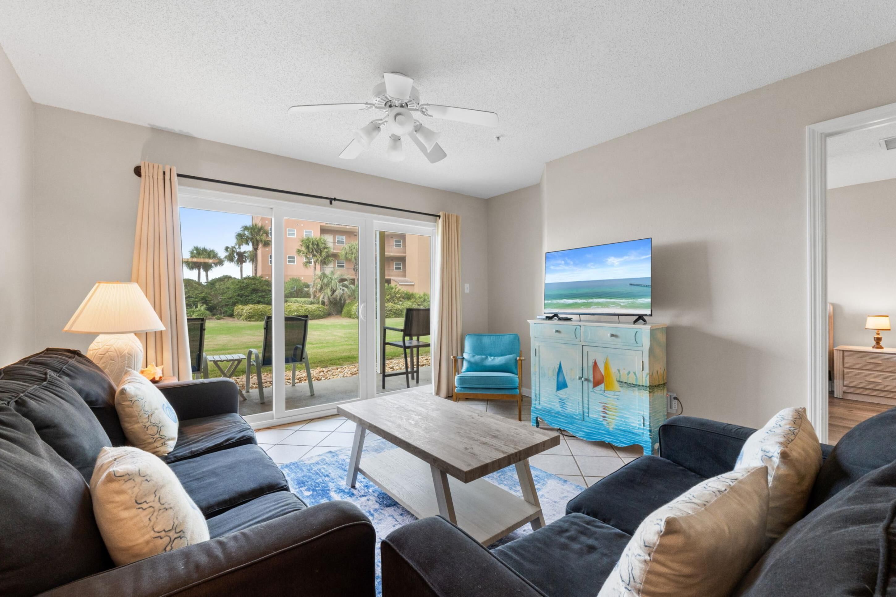 A living room with a sofa, a coffee table, a TV, and a view of a golf course through the sliding glass door.