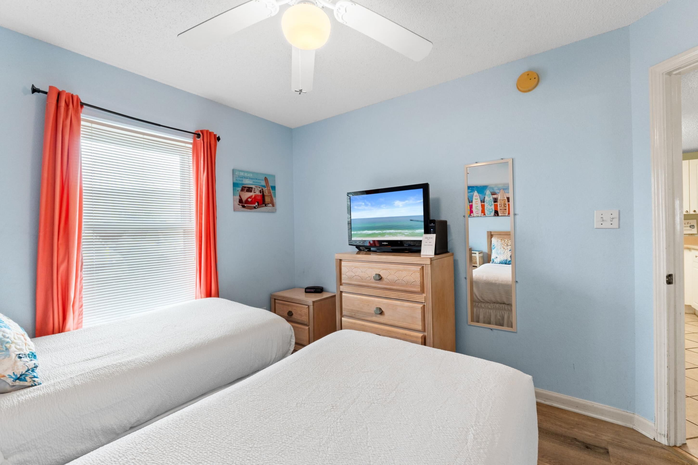 A bedroom with two beds, a TV, a dresser, and a ceiling fan.