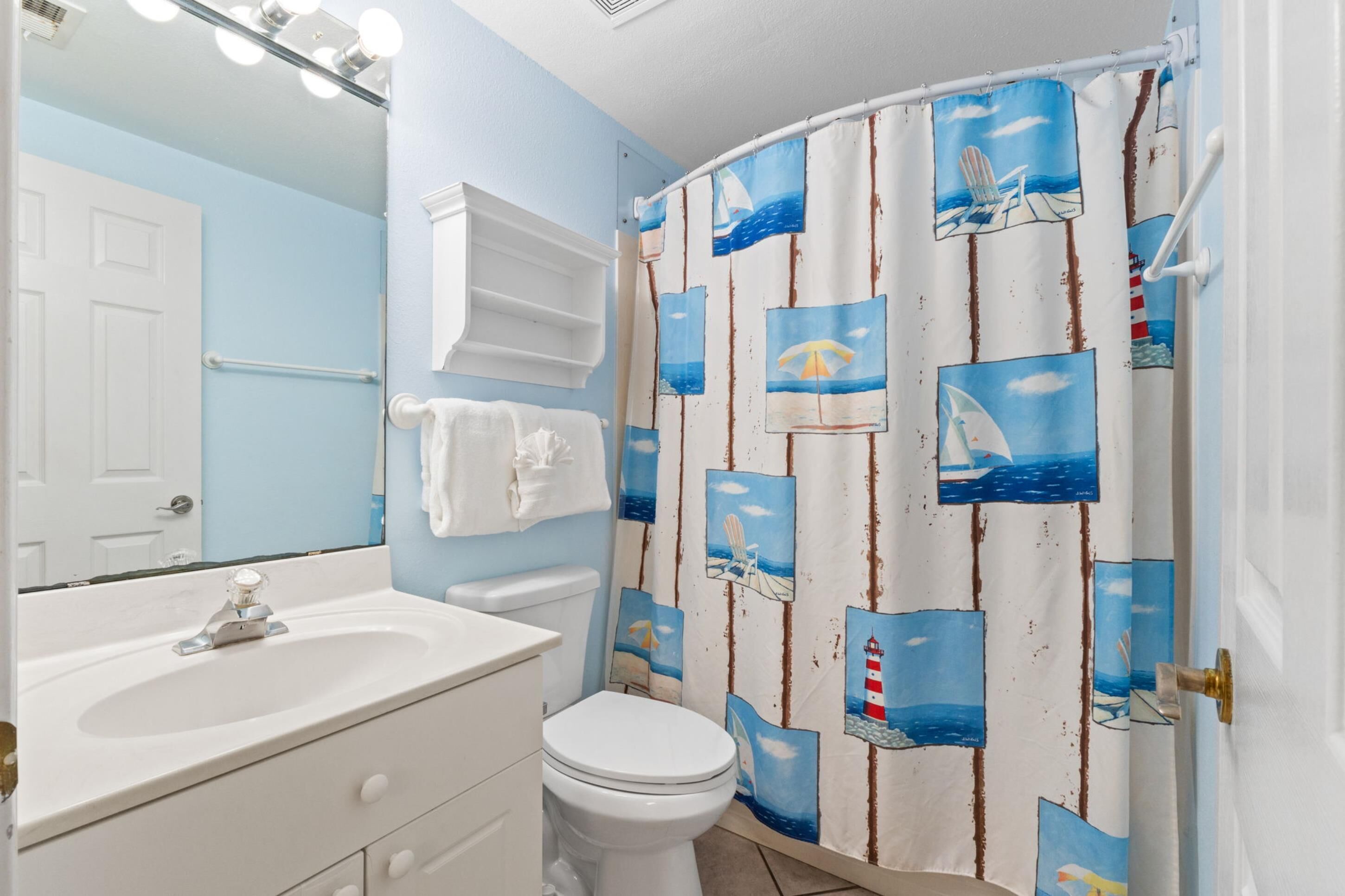 A bathroom with a white sink, a toilet, a mirror, and a shower curtain with nautical designs.