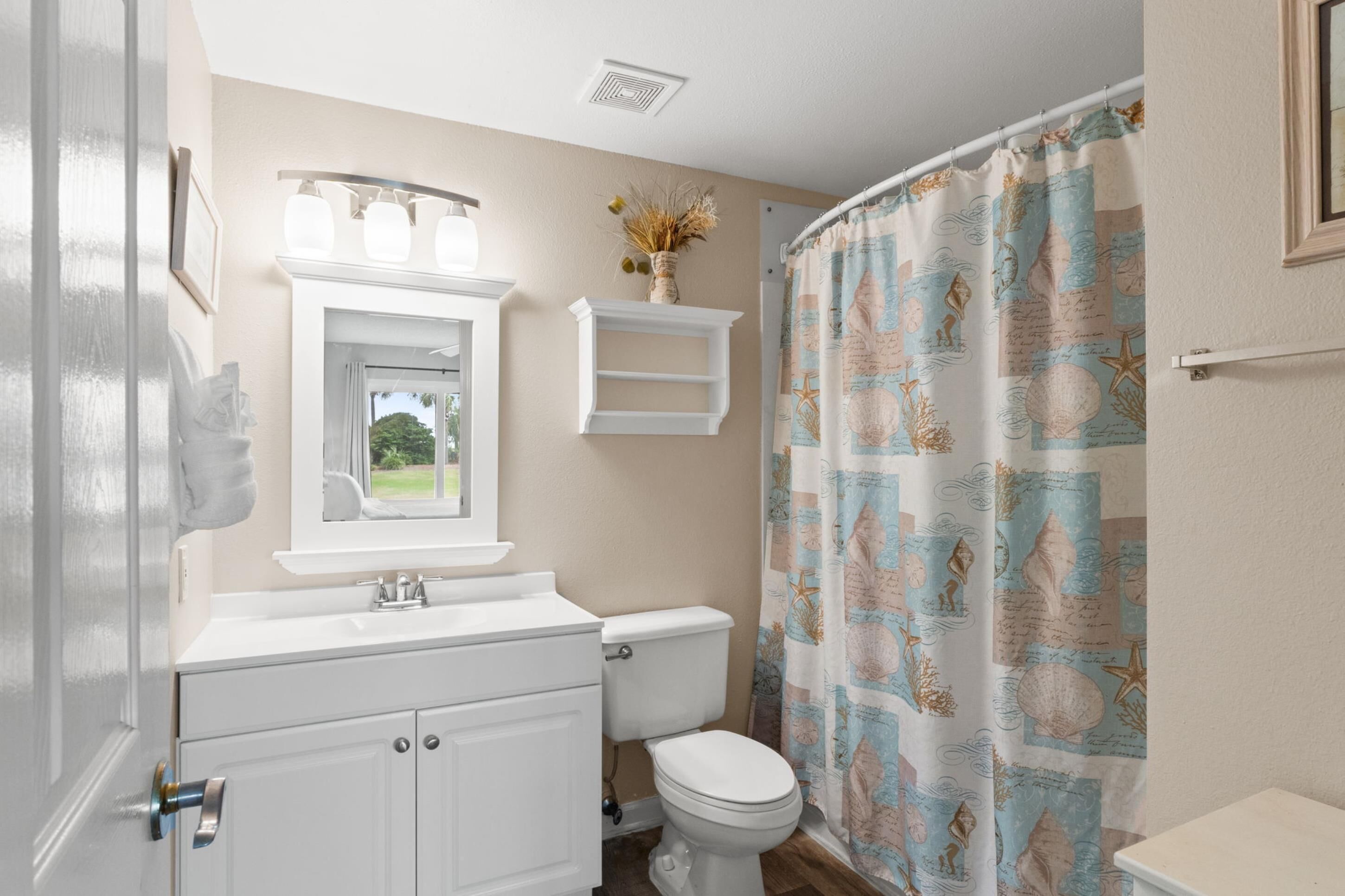 A bathroom with a toilet, sink, vanity, and a shower curtain with a nautical theme.