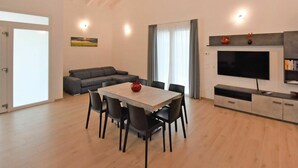 A modern living room with a dining area, a grey sofa, a flat-screen TV, and a fireplace mantel. - Wonderful private villa for 6 guests with A/C, pool, WIFI, TV and balcony (Venice)