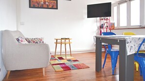 Una sala de estar con un sofá, una mesita, un tapete colorido y un televisor montado en la pared.