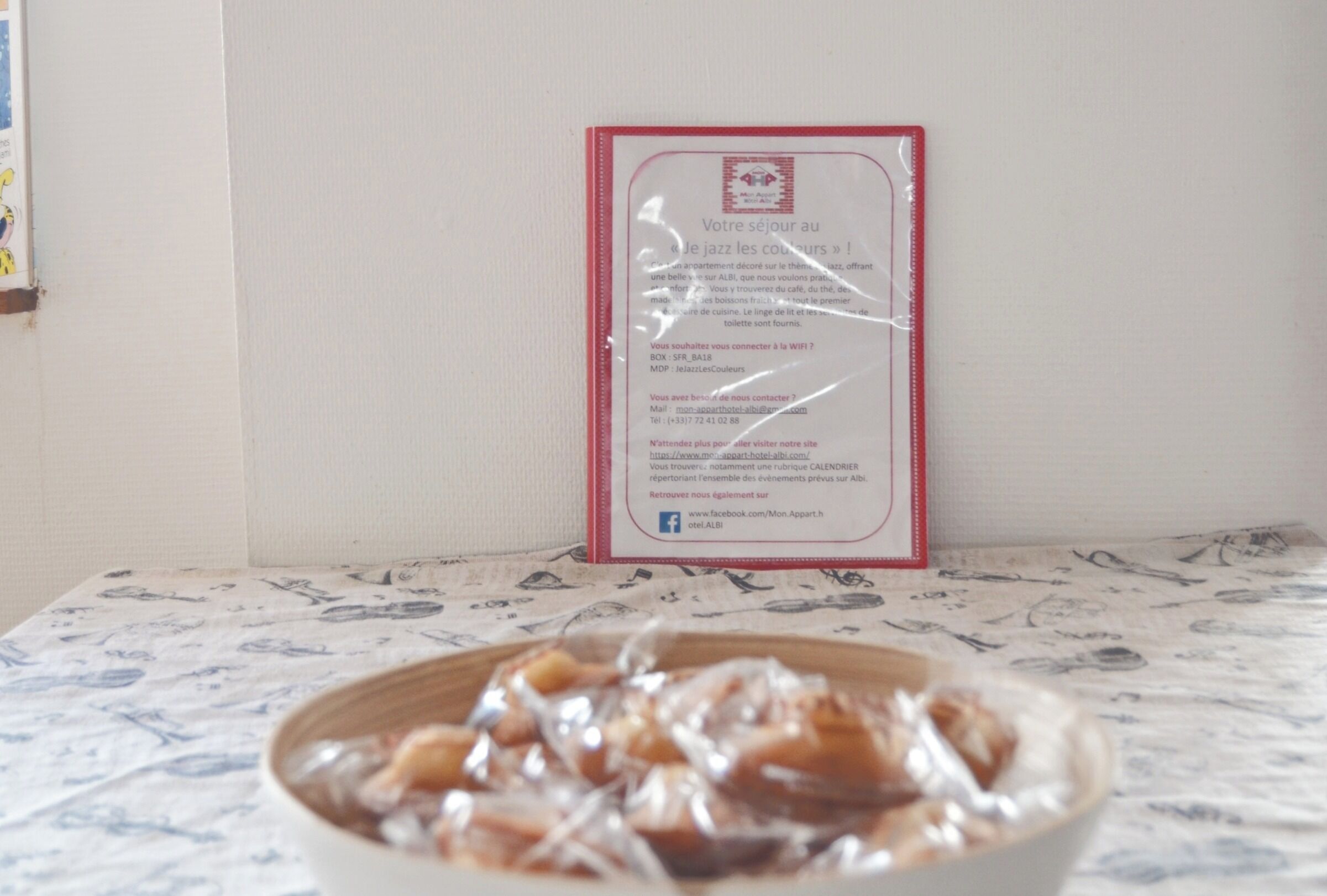 Ein gerahmtes Willkommen-Schild mit Kontaktinformationen und einer Website-URL, eine Schüssel mit Essen auf einem Tisch mit gemustertem Tischläufer.