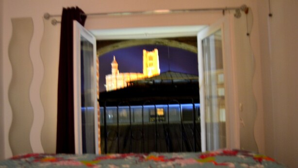 Un dormitorio con cama, ventana con cortinas y vista a un edificio con torre.