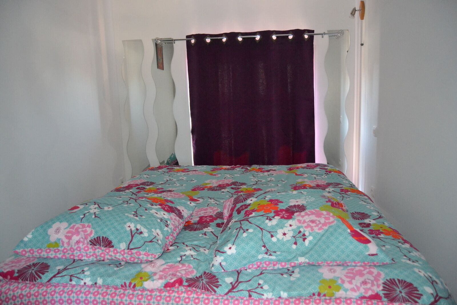 Un letto con una coperta a fiori, una testiera bianca e una tenda viola.