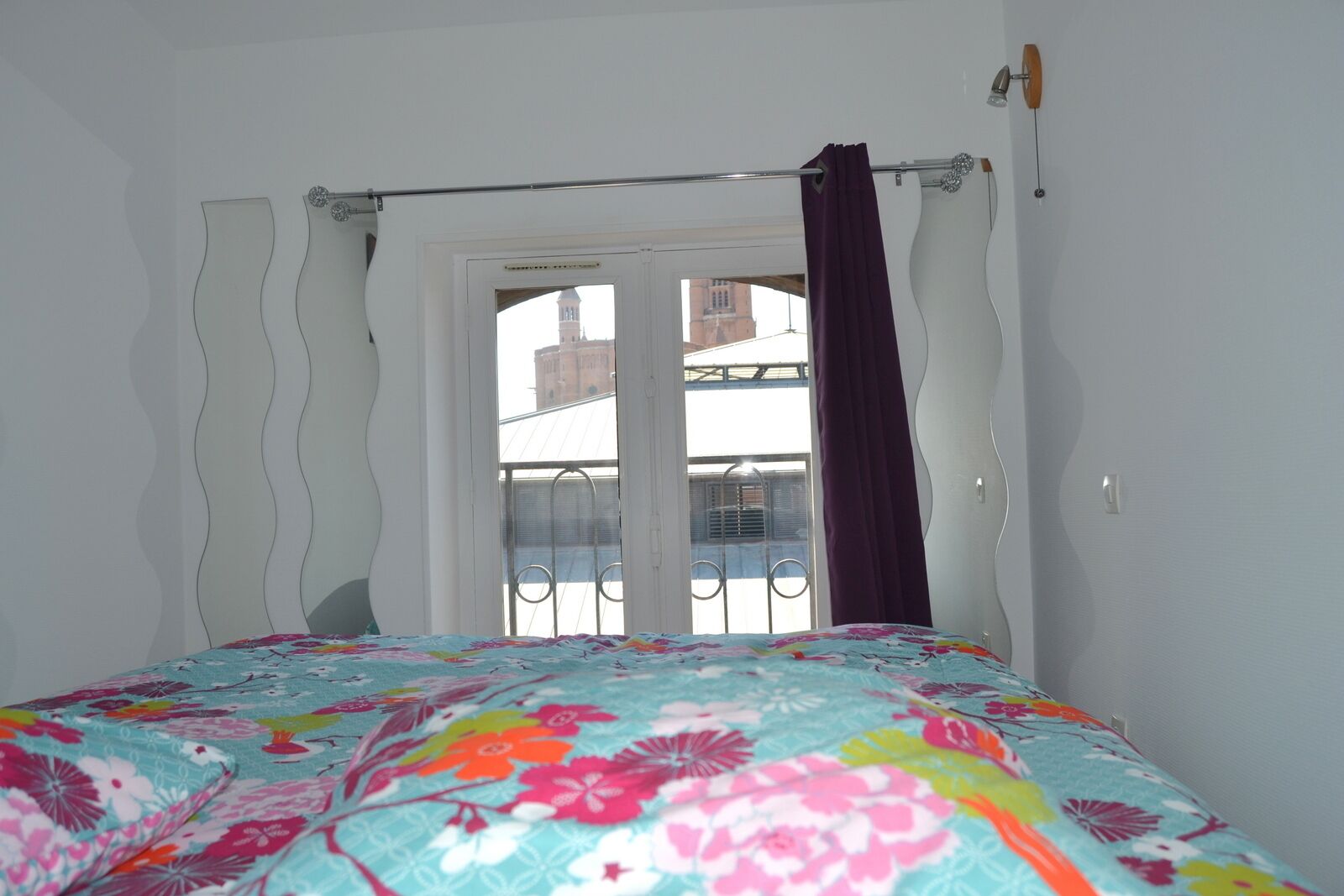 Una camera da letto con un letto, una finestra che si affaccia su edifici e una tenda.