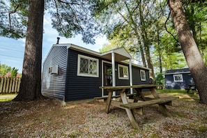 A small cabin with a porch and a picnic table, surrounded by trees. - Hidden Haven Cottages (Lake City)