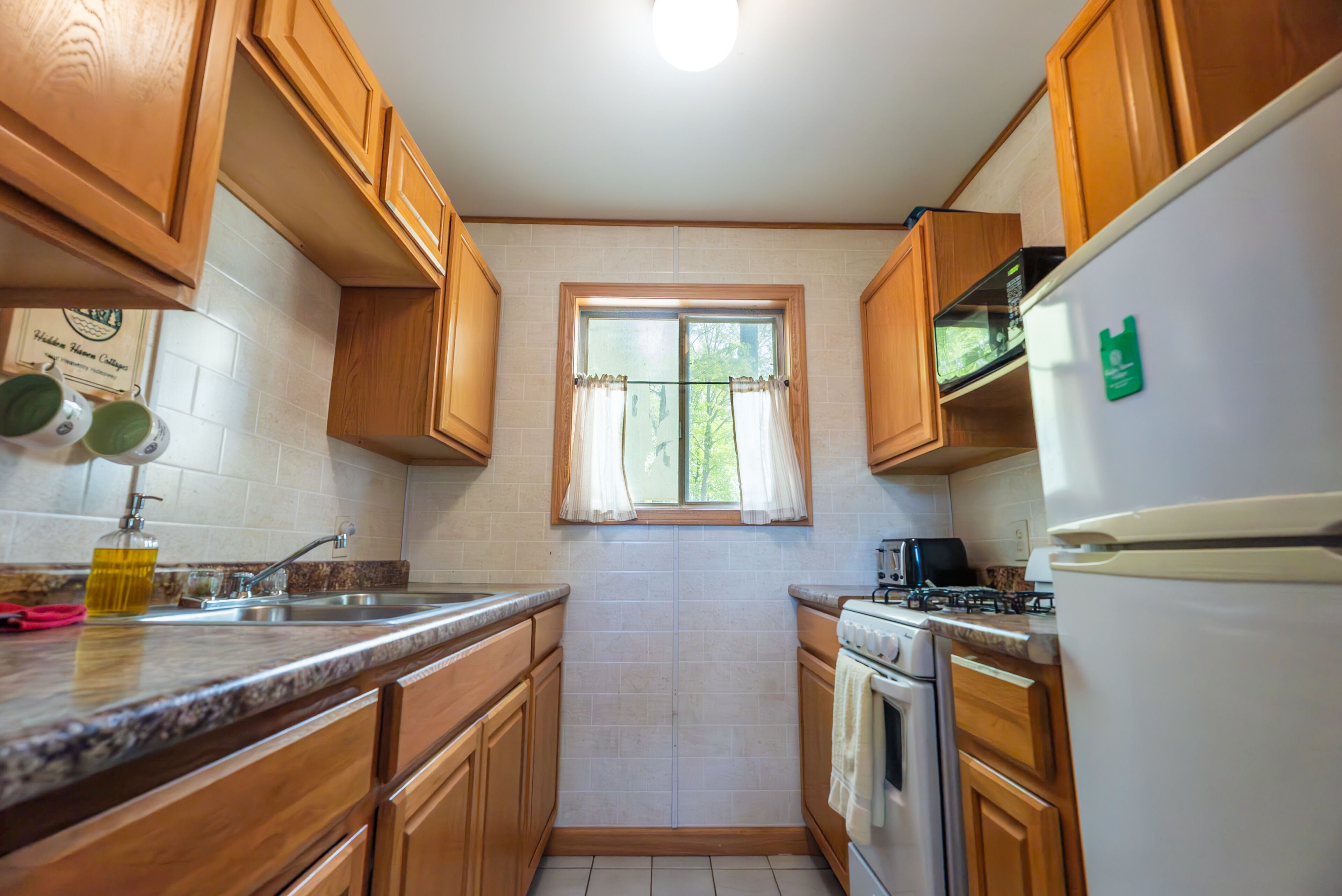 A kitchen with wooden cabinets, a window with curtains, a sink, a stove, and a refrigerator.