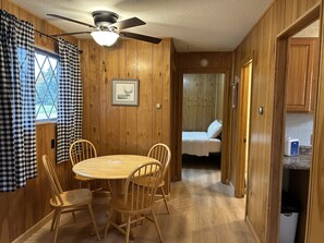 A wooden cabin with a dining area, a bed, and a ceiling fan.