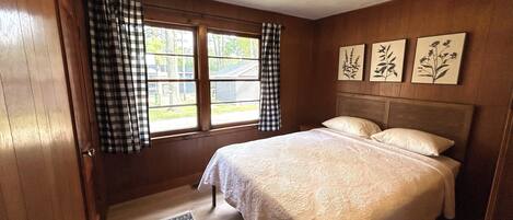 A bedroom with a large bed, a window with curtains, and wall-mounted artwork.