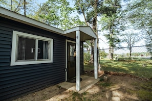 A single-story house with a dark exterior, a front door, and a window with a checkered curtain. - Hidden Haven Cottages (Lake City)