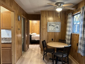 A wooden interior with a dining table, chairs, a ceiling fan, a bed, and a painting on the wall. - Hidden Haven Cottages (Lake City)
