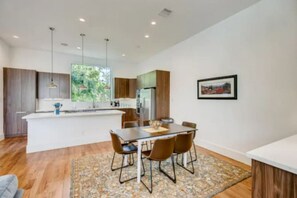 A modern kitchen with a central island, dining area with chairs, and a large window.