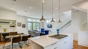 Une cuisine moderne dotée d’un grand îlot central, de luminaires suspendus et offrant une vue sur l’espace de vie.