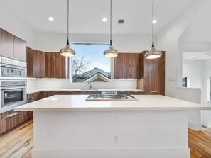 A modern kitchen with a large island, pendant lighting, and wooden cabinetry.