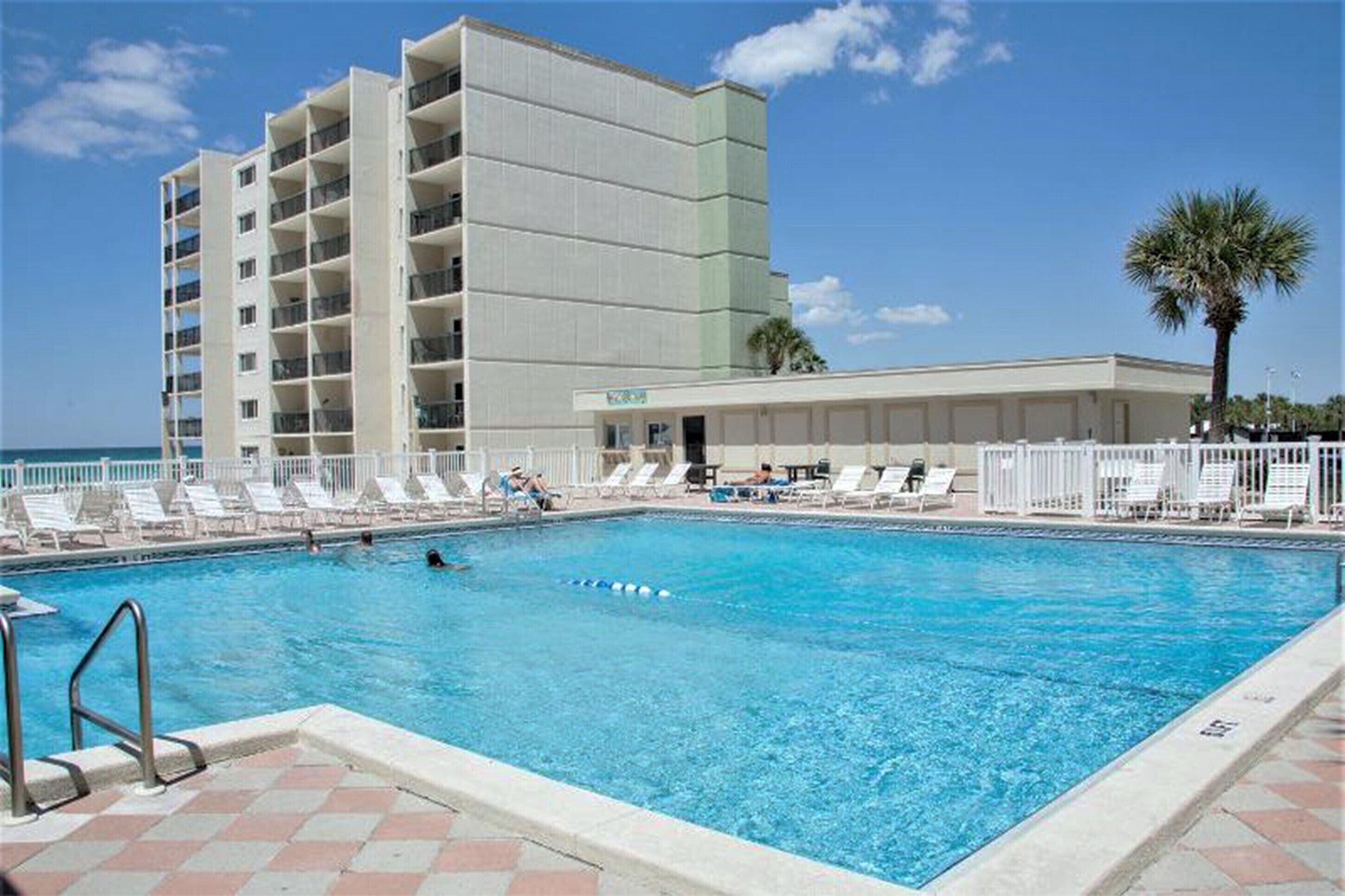 Una piscina con sillones de descanso y un edificio con varios balcones al fondo.