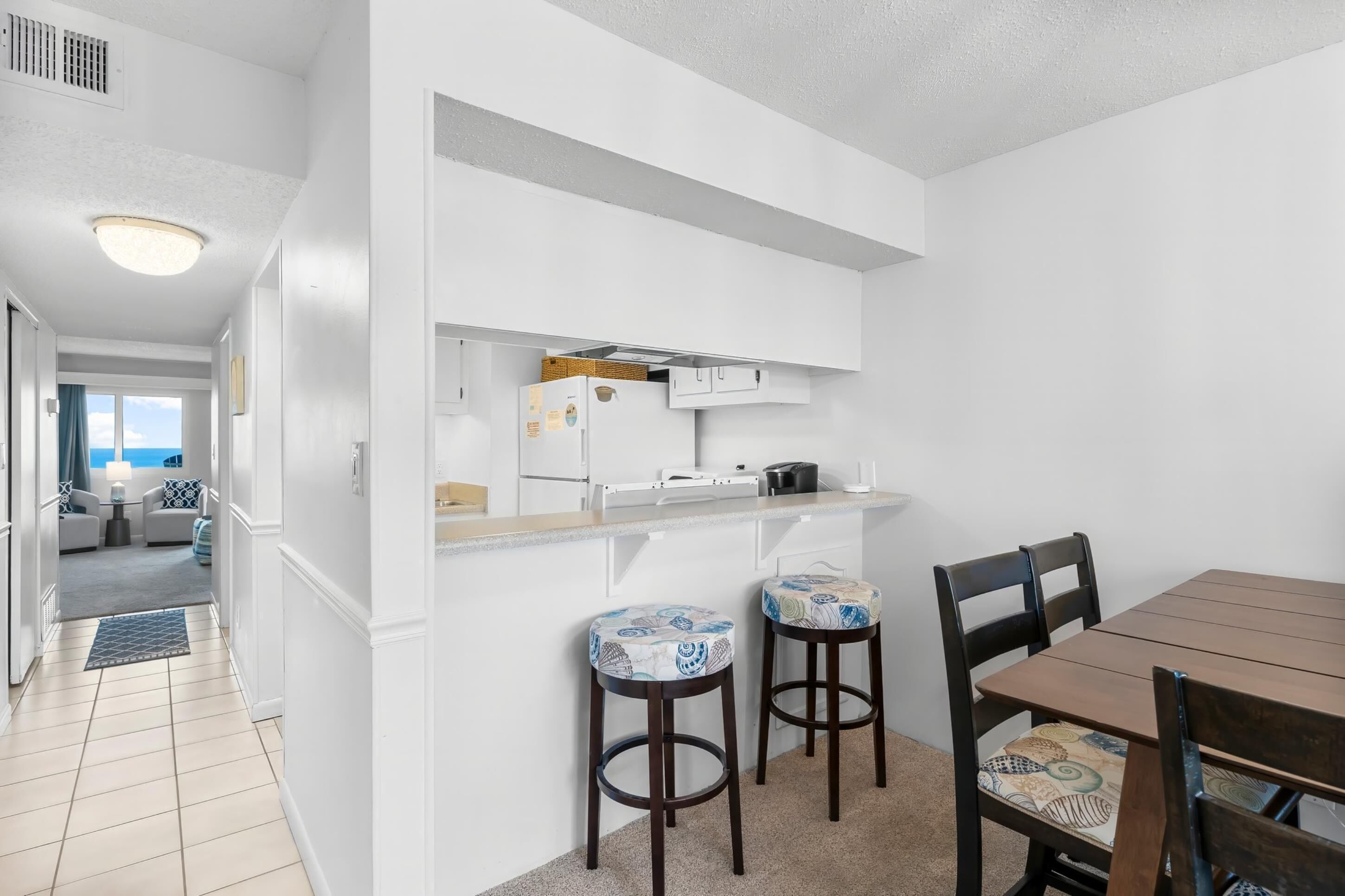 Una cocina compacta con gabinetes blancos, una encimera y dos taburetes de bar.